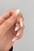 Gold huggie earring with clear stones and a pale pink heart-shaped cubic zirconia charm
