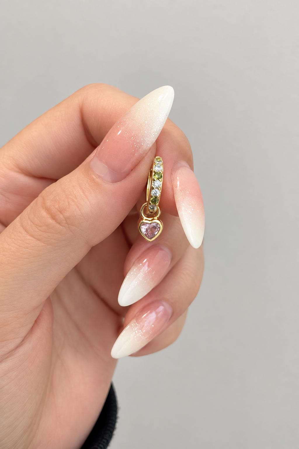 Close-up angled view of gold huggie earring with pale pink heart-shaped cubic zirconia charm