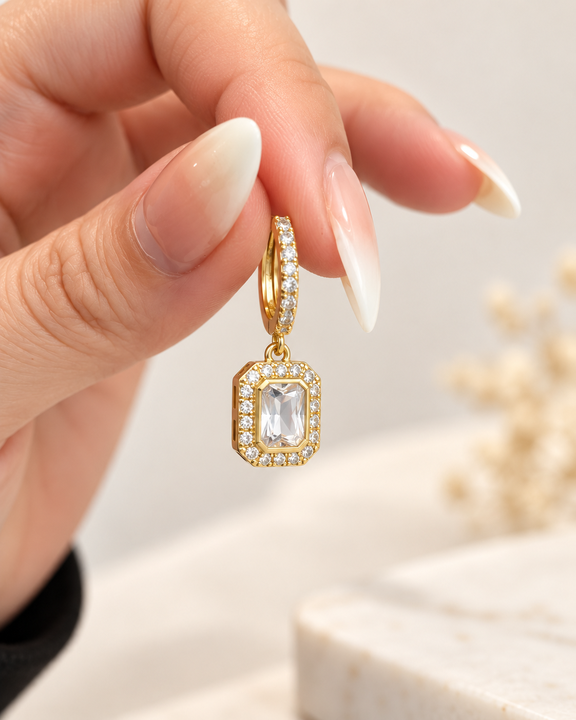 Gold huggie earring with clear emerald-cut crystal drop, close-up lifestyle view