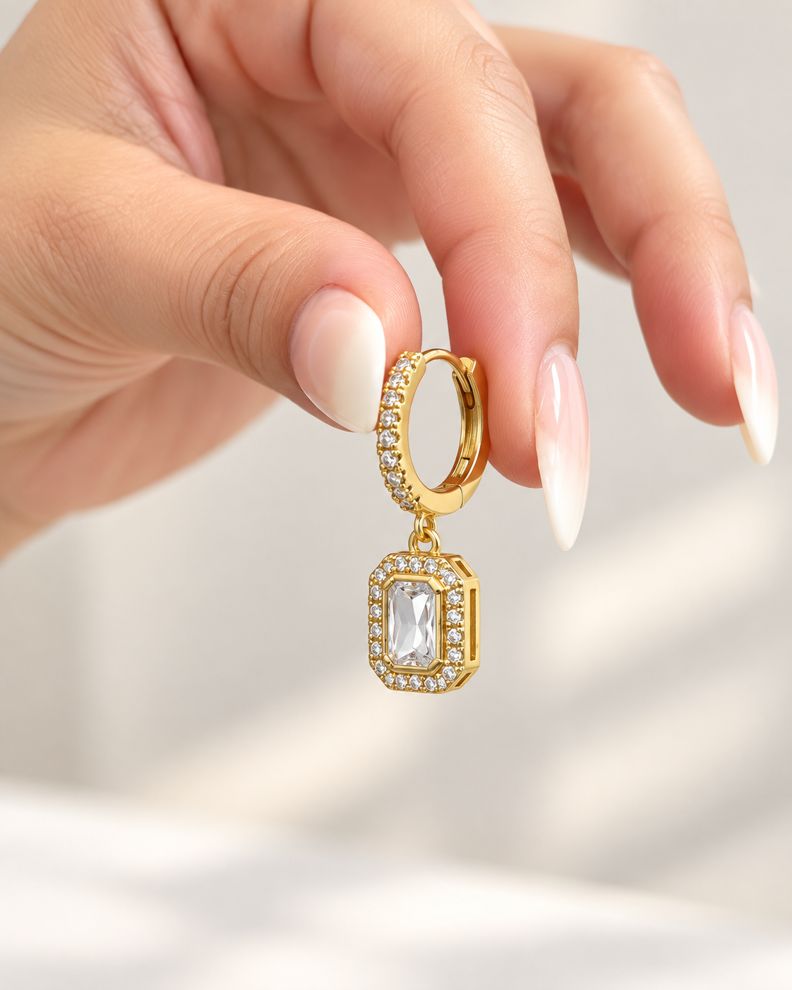 Angled close-up of gold hoop earring with clear rectangular crystal pendant
